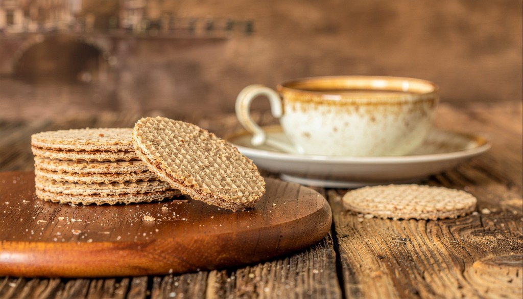A Dutch stroopwafel on a plate beside a cup of coffee.
