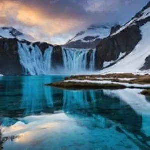 Stunning frozen waterfall and crystal clear alpine lake in the snowy mountains